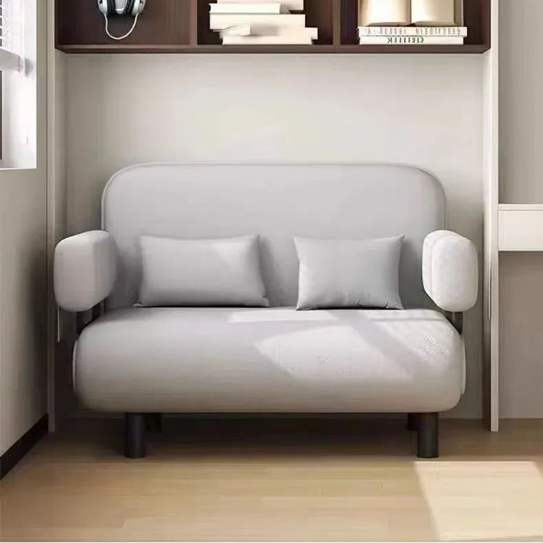 Modern gray sofa in a minimalistic room with a bookshelf and desk.