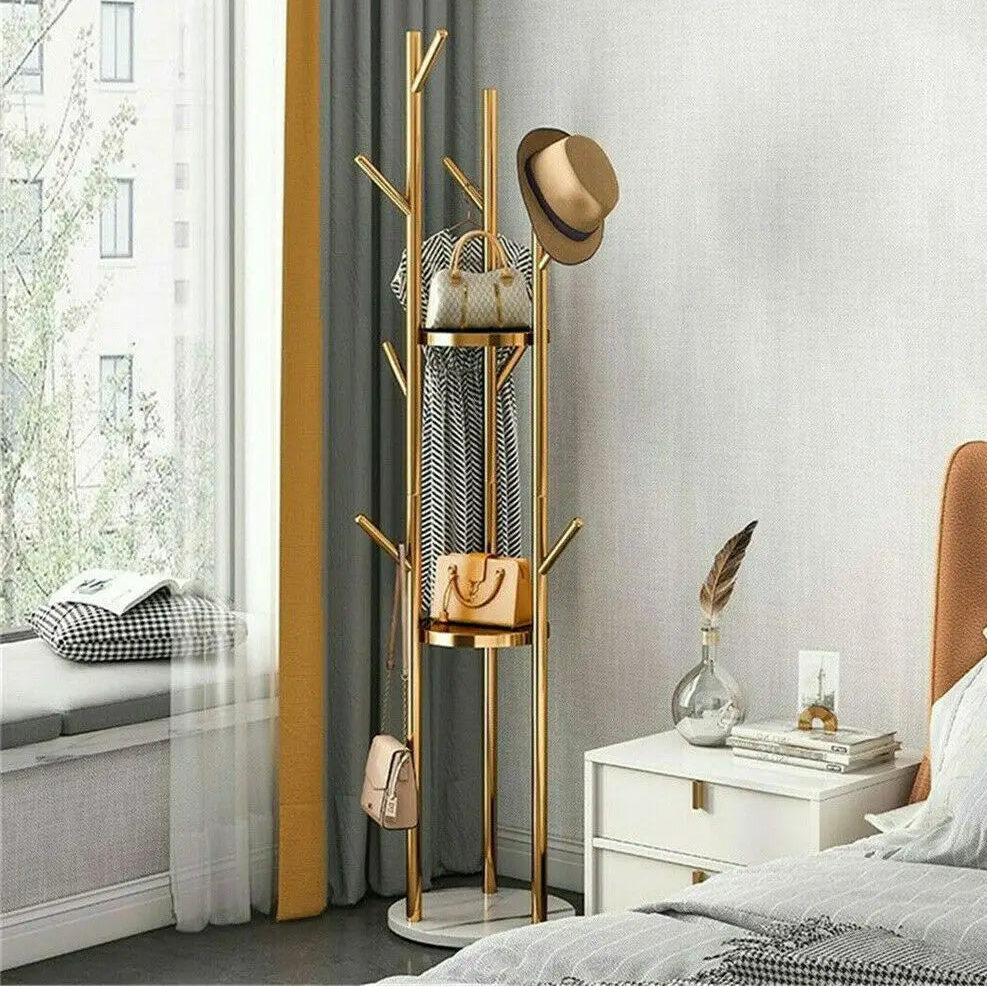 A modern style freestanding marble metal coat rack with three storage shelves and nine hooks, with a golden iron frame and white artificial marble base, placed in a room beside a window.