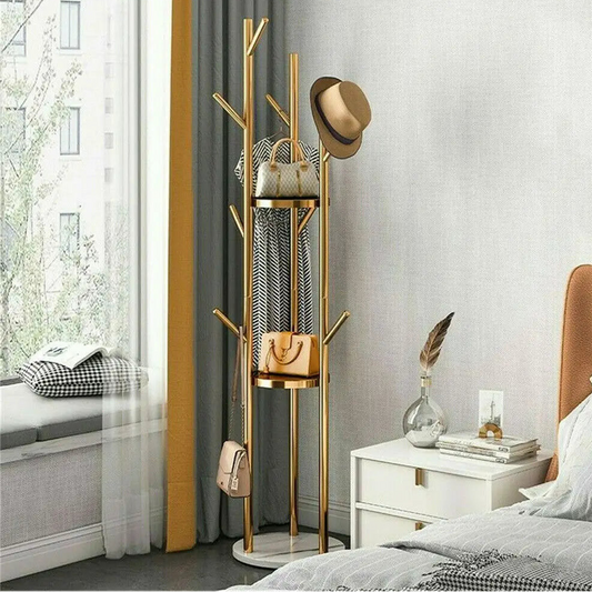 A modern style freestanding marble metal coat rack with three storage shelves and nine hooks, with a golden iron frame and white artificial marble base, placed in a room beside a window.