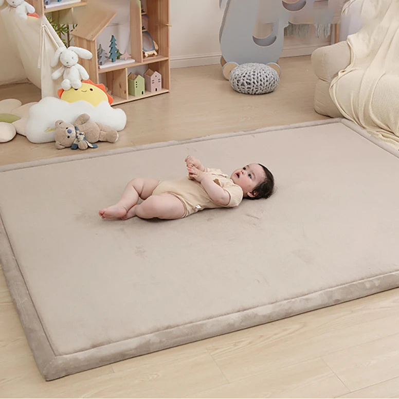 Baby lying on a large beige mat in a room with toys and furniture.