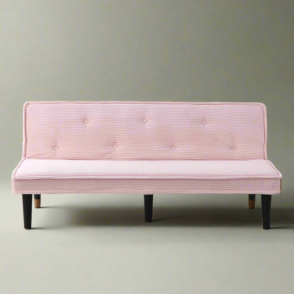 Pink sofa bed in a room with a white wall and wooden floor.