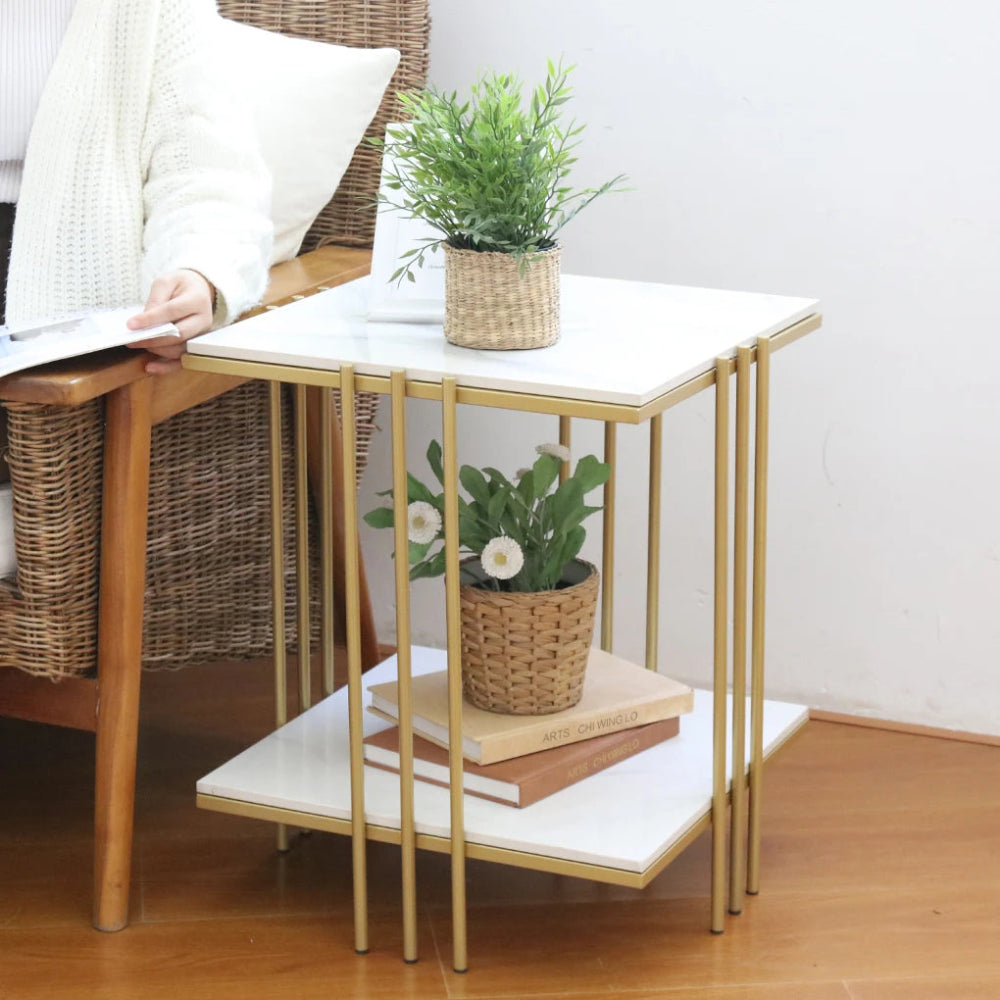 Small side table with marble top and gold legs, featuring a plant and books on a wooden floor.