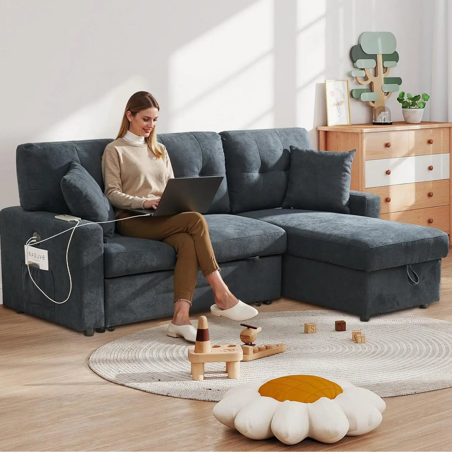 Woman using a laptop on a gray sectional sofa in a bright living room.