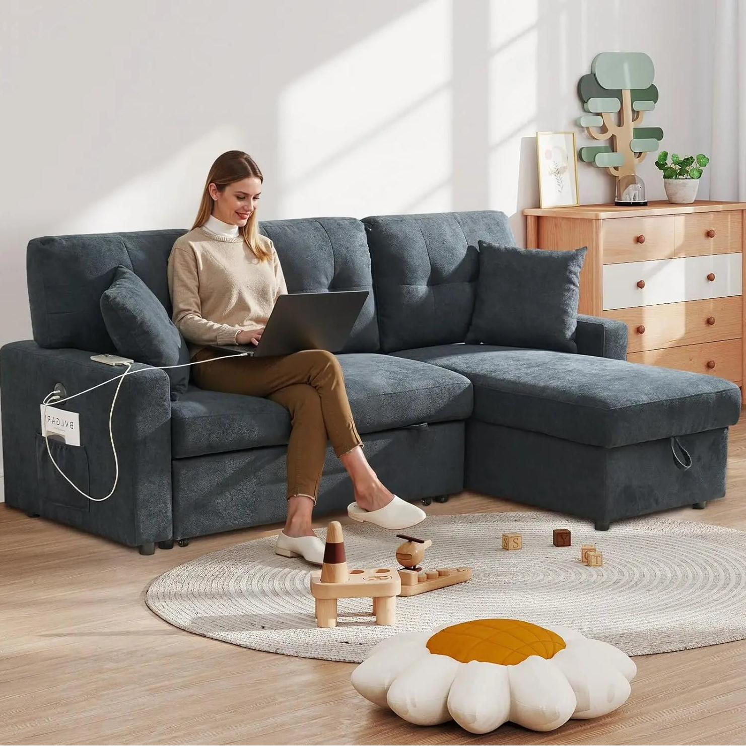 Woman using a laptop on a gray sectional sofa in a bright living room.
